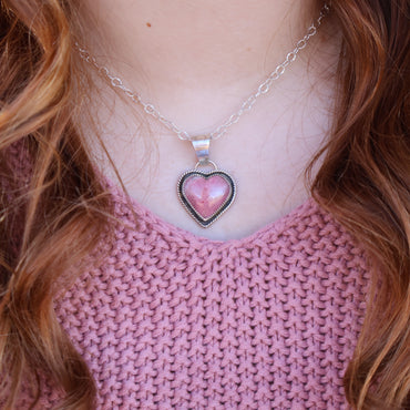 Person wearing a pink sweater and a necklace with a heart-shaped pendant