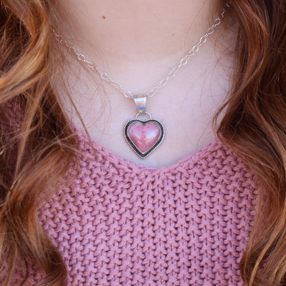 Person wearing a pink sweater and a necklace with a heart-shaped pendant