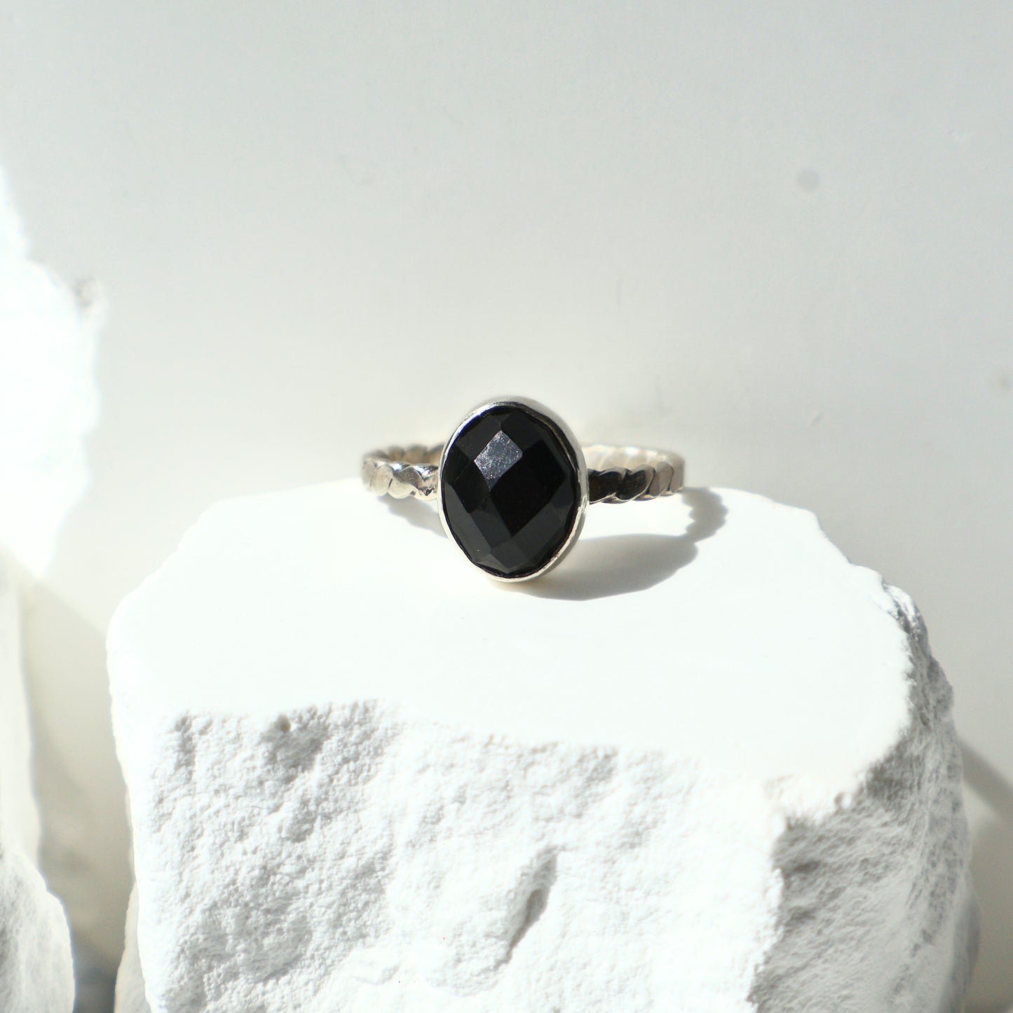 Silver ring with a black onyx gemstone on a white stone surface