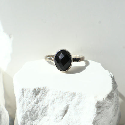 Silver ring with a black onyx gemstone on a white stone surface